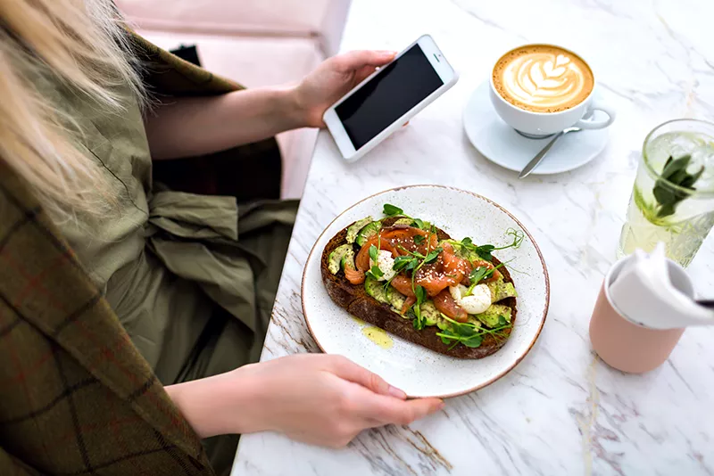 woman-eating-her-tasty-brunch-on-hipster-cafe-top-view-of-marble-table-salmon-avocado-toast-coffee-and-sweet-tasty-cheesecakes-enjoying-her-breakfast-(2)